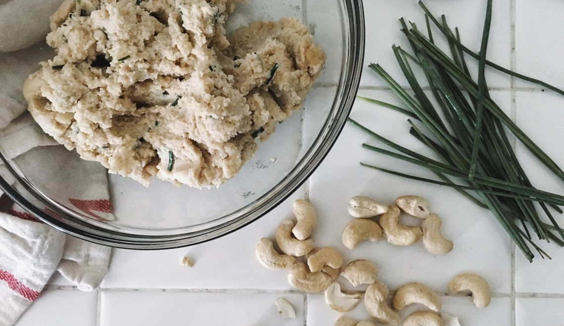 A bowl of cashew cheese with a cashews and chives on kitchen counter.