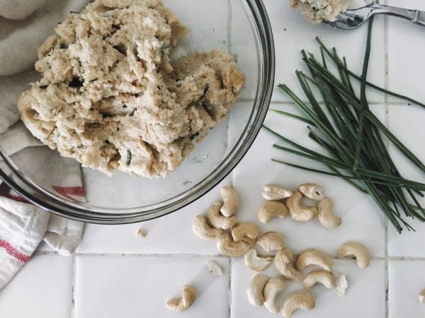 A bowl of cashew cheese with a cashews and chives on kitchen counter.