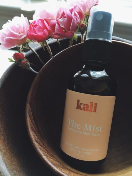 Kali rosewater mist in wood bowl with pink roses.