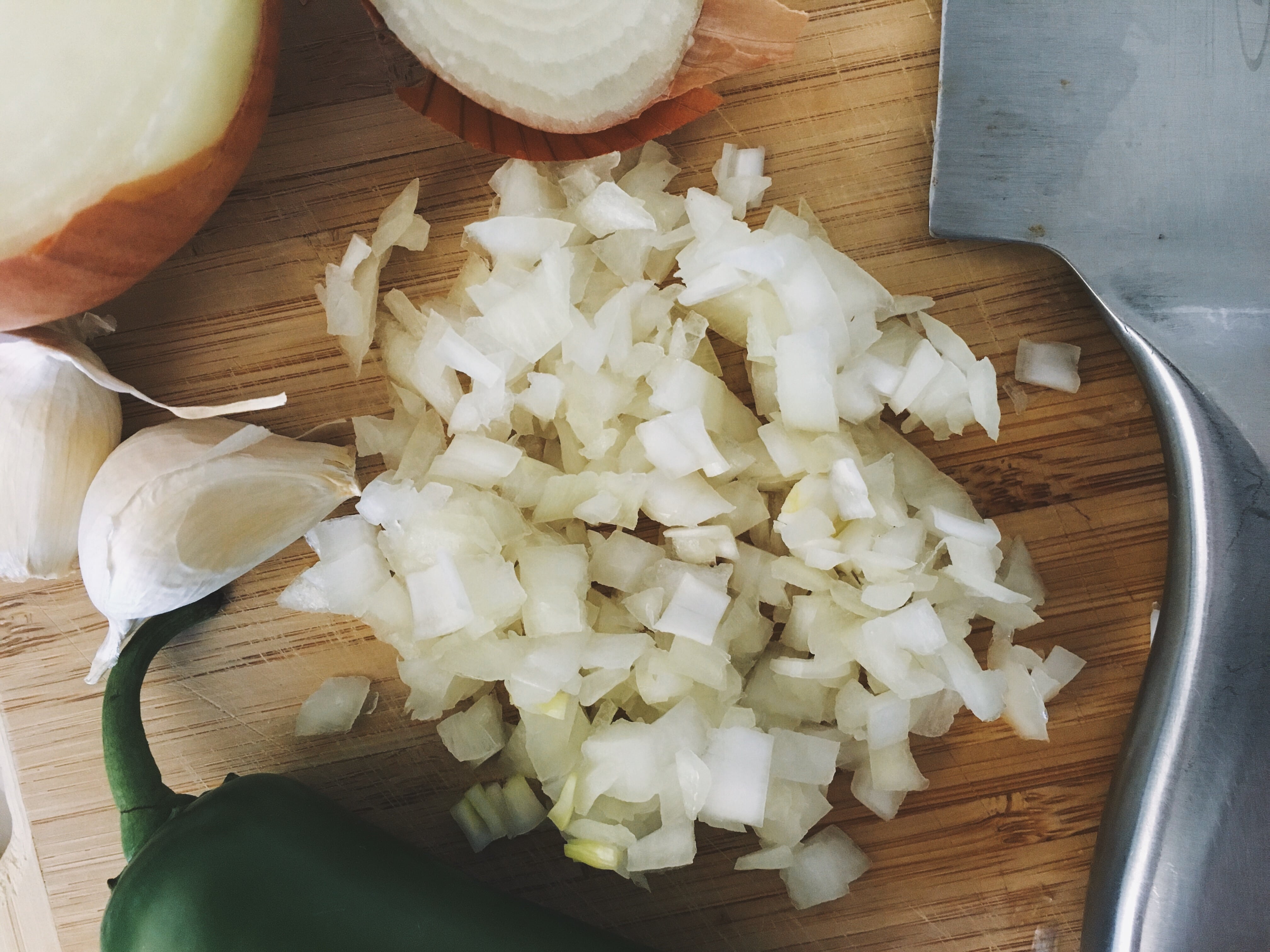 Diced yellow onion with garlic cloves and jalepeno on a wood cutting board
