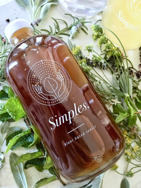 a beautiful Simples Tonics bottle resting on a bed of fresh herbs